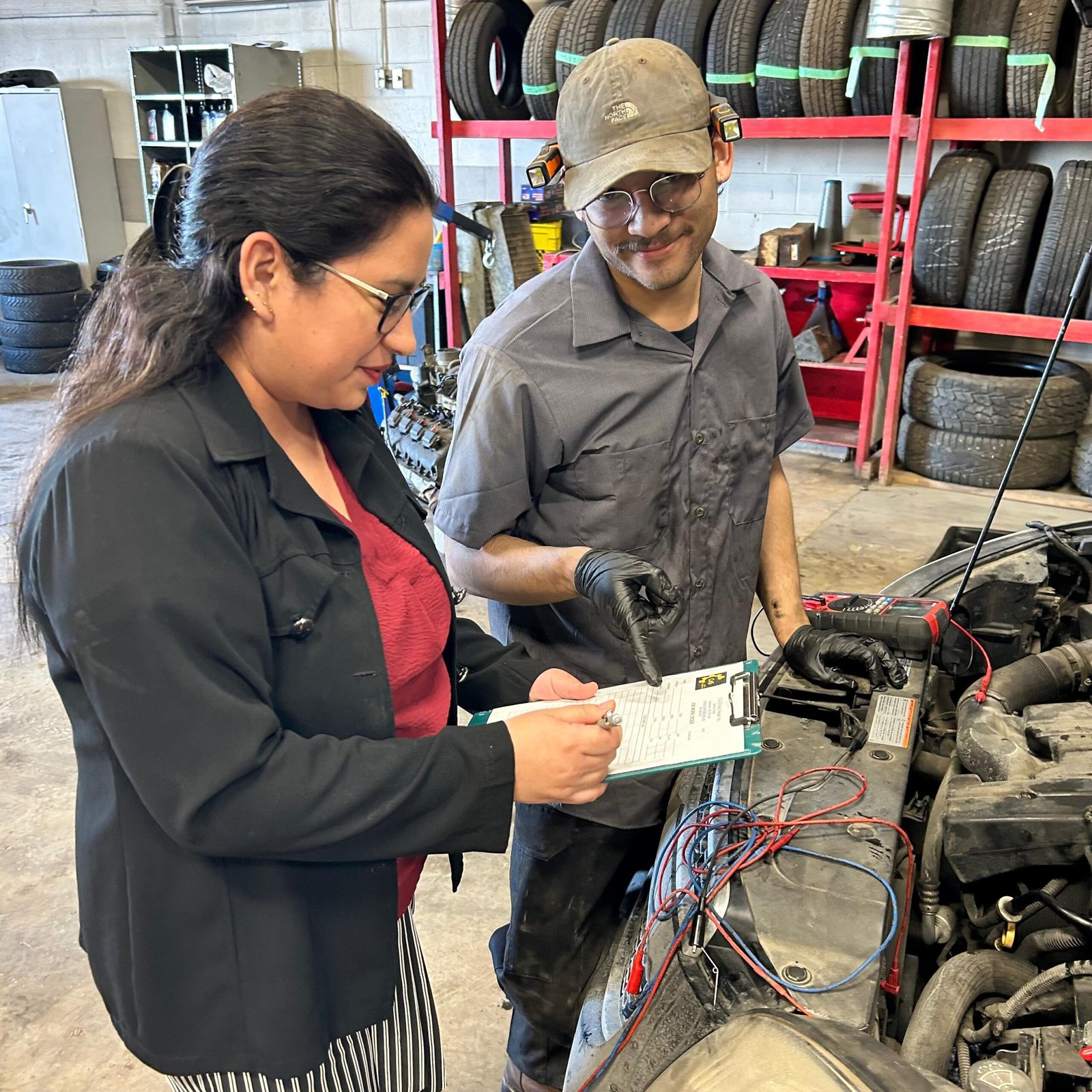 Vehicle scheduled maintenance inspection Two technicians inspecting a car with the hood open, using a checklist clipboard